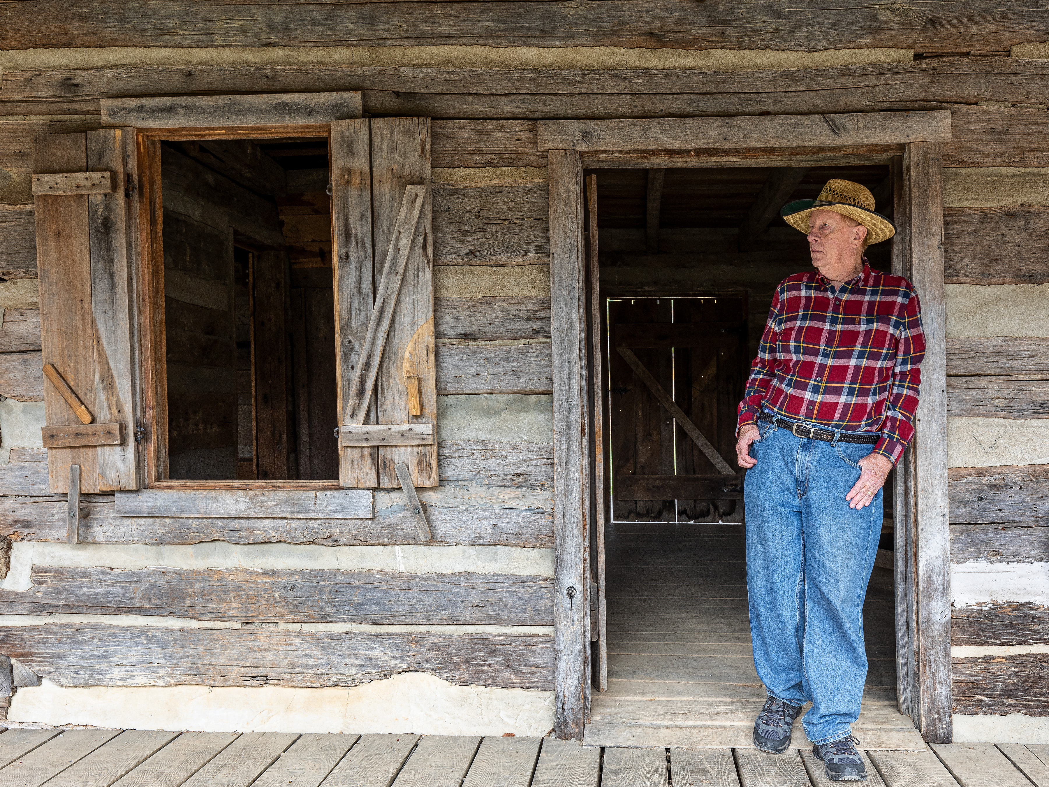 An older man stands in the doorway of a cabin